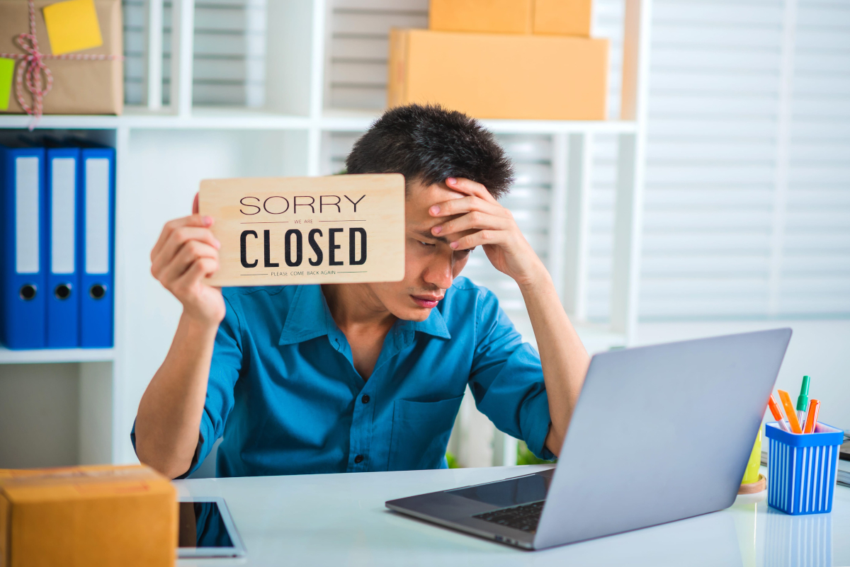 small business owner holding up a sorry closed sign because his laptop is not working due to an IT outage